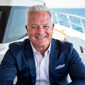 Smiling middle-aged man with silver hair in navy suit and white shirt on yacht with ocean backdrop