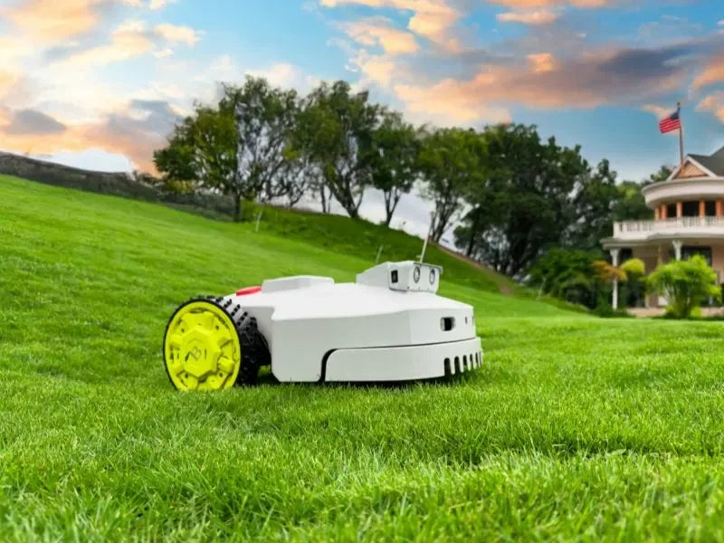 Robotic lawn mower on a green lawn at sunset, with a house, trees.